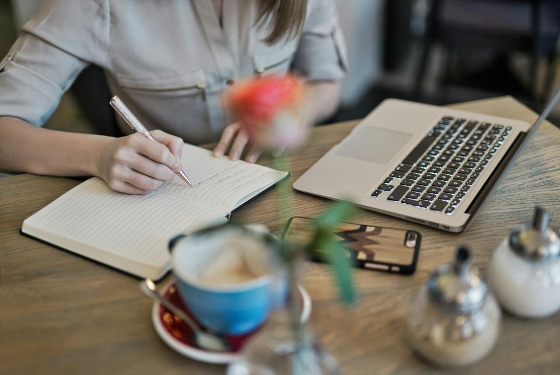 A person writing in their journal next to their laptop.